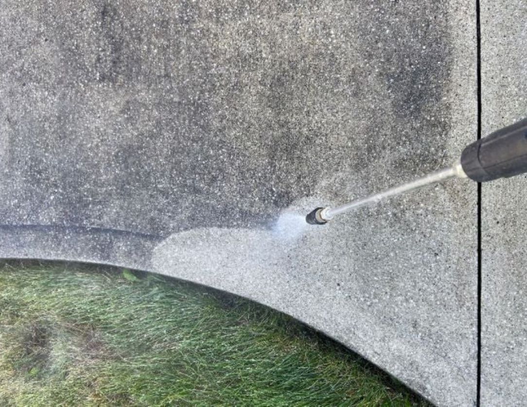 A close-up of a pressure washer cleaning a concrete surface, showcasing Concrete Pressure Washing Services to remove stains and restore the surface's appearance.
