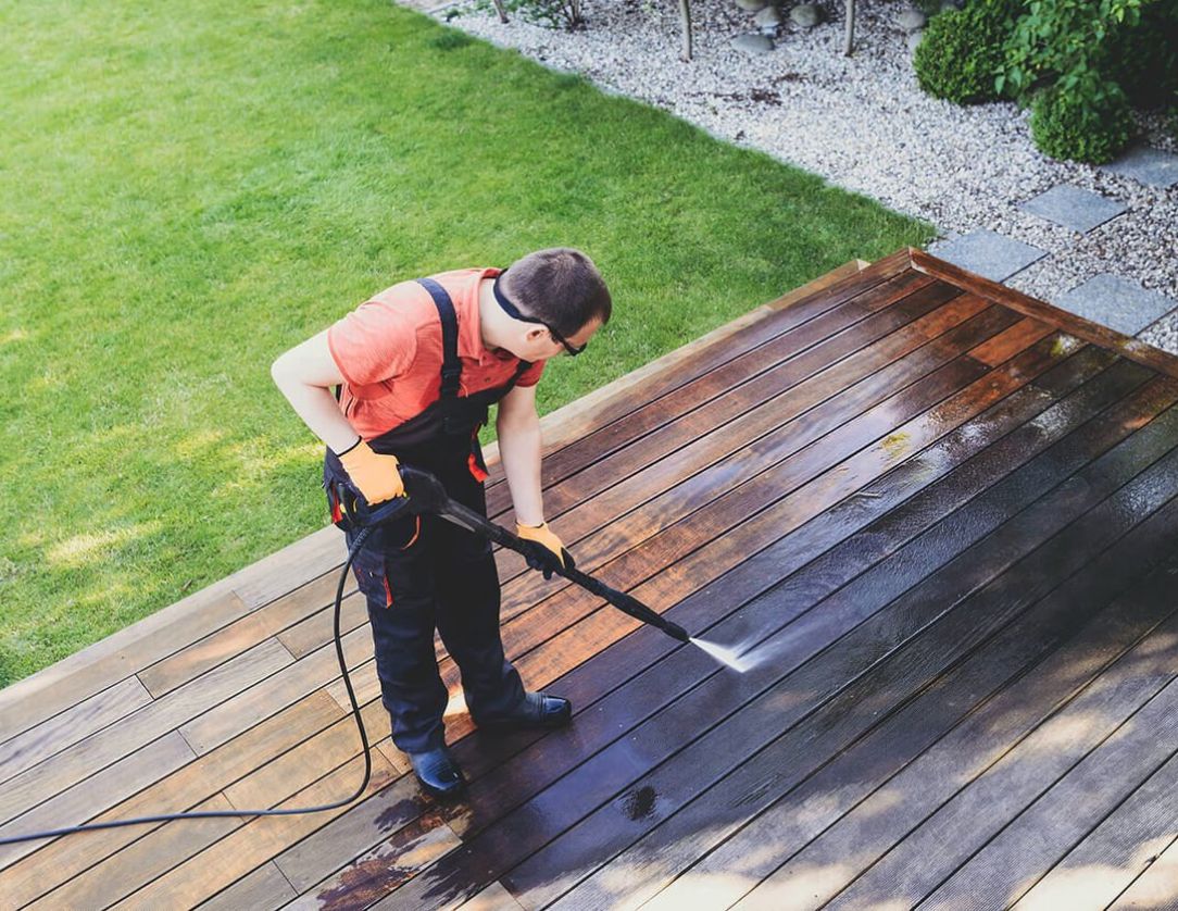 A professional using a pressure washer to clean a wooden deck, demonstrating Decks Pressure Washing Services for restoring the appearance of outdoor surfaces.