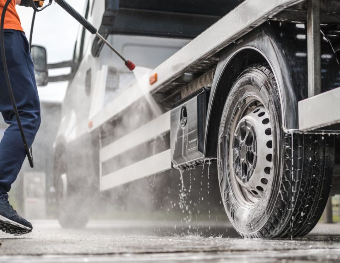 A professional using a pressure washer to clean the wheels and body of a commercial vehicle, showcasing Fleet Pressure Washing Services for maintaining a clean and professional fleet appearance.