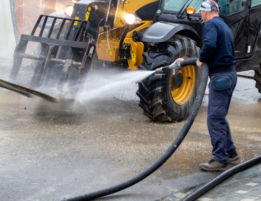 A professional using a pressure washer to clean heavy equipment, highlighting Heavy Equipment Pressure Washing Services to maintain machinery performance and appearance.