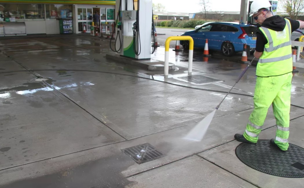 A worker performing Gas Station Washing Services using a high-pressure washer to clean the concrete surface around fuel pumps, ensuring a spotless and safe environment.