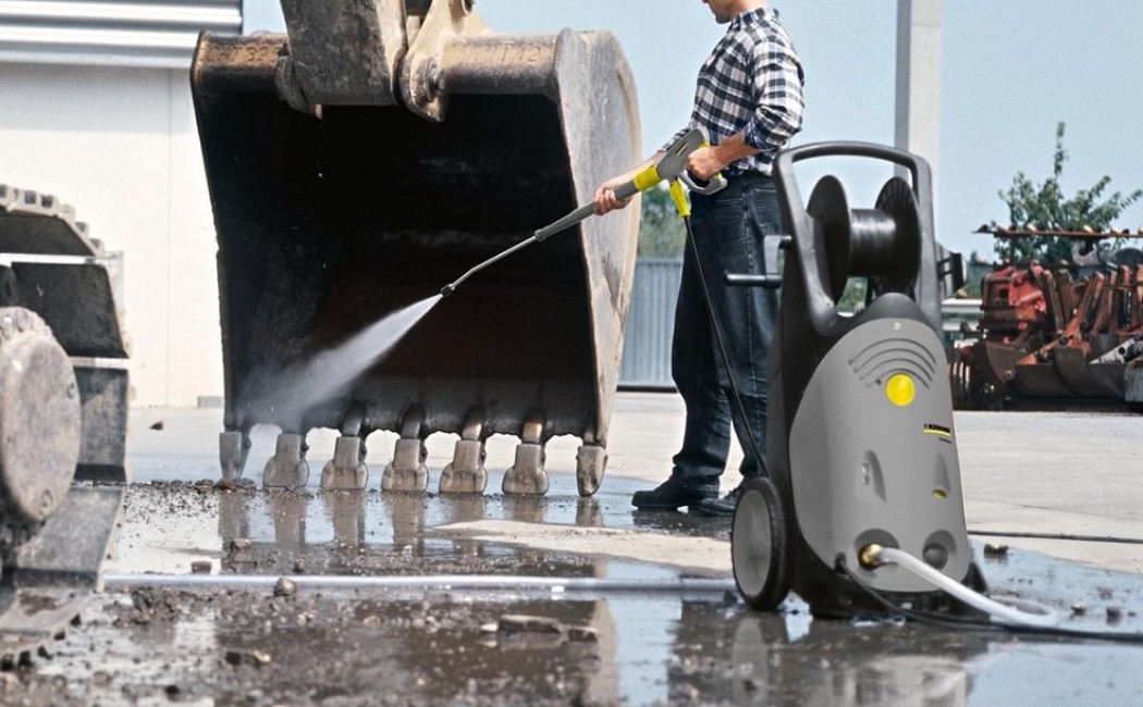 A worker using a pressure washer to clean an excavator at a construction site, showcasing the services of a Pressure Washing Excavator Company.