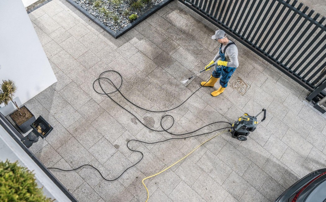 A person in protective gear power-washes a dirty driveway, illustrating thorough Driveway Washing Services.