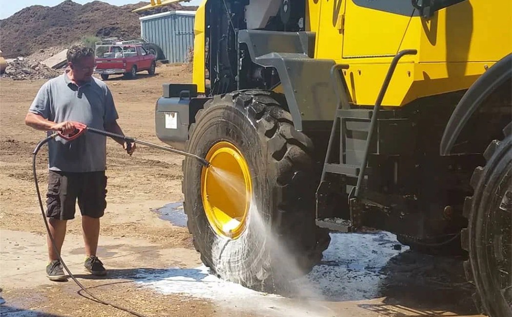 A worker uses a pressure washer to clean the large tire of a construction vehicle, showcasing the services of a Heavy Equipment Pressure Washing Company.