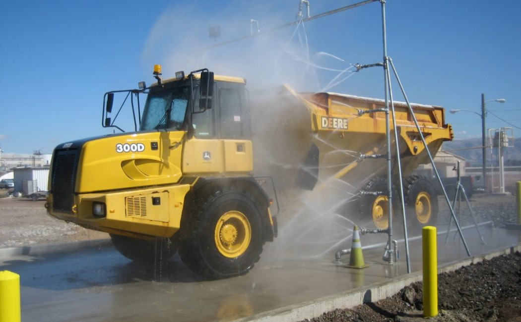 A large yellow dump truck is cleaned by an automated spray system at an outdoor wash station, demonstrating professional Heavy Duty Washing Services.