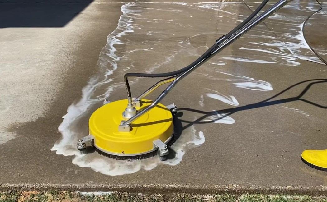 A yellow pressure-washing surface cleaner glides over a driveway, highlighting efficient Driveway Washing Services.