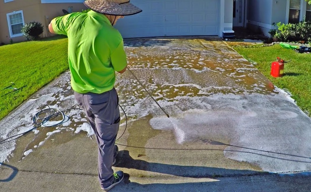 A worker uses a pressure washer to clean a soapy concrete driveway, demonstrating professional Driveway Washing Services in action.