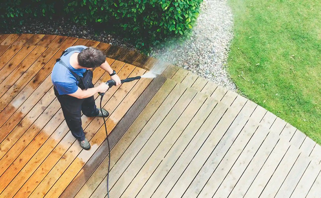 A professional worker pressure washing a wooden backyard deck, restoring its clean finish as a Residential Deck Washing Company service.