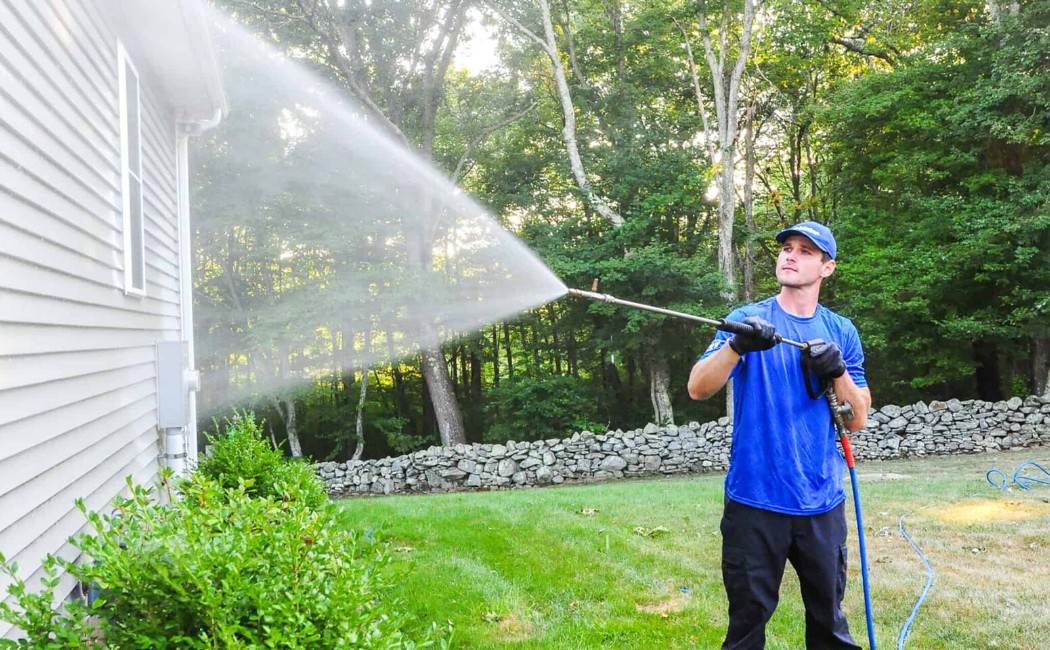 A Residential Washing Company technician is pressure washing the exterior siding of a home, removing dirt and grime.