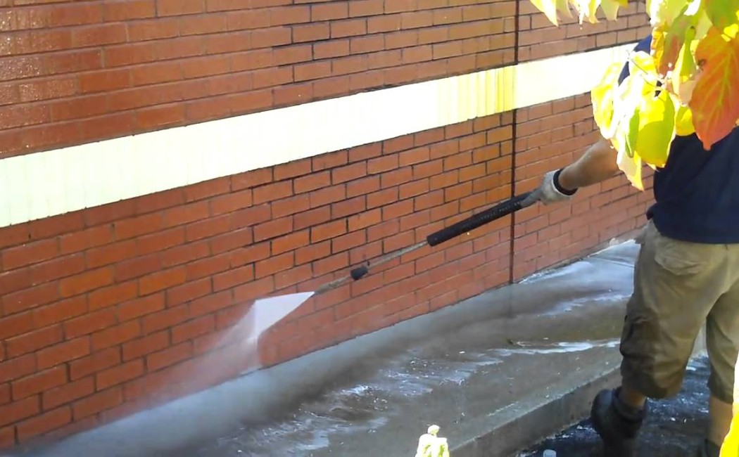 Professional cleaner pressure washing a brick exterior wall to remove dirt and stains, showcasing reliable Building Washing Services for long-lasting surface protection.