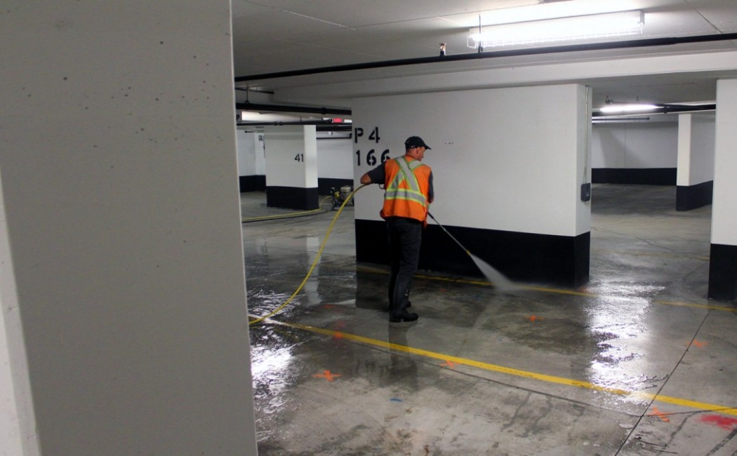 Worker using high-pressure equipment to clean a parking garage floor, illustrating Commercial Pressure Washing Services for maintaining clean and safe commercial spaces.
