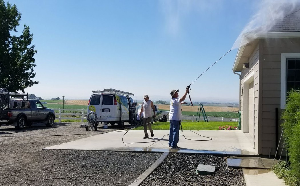 Commercial Pressure Washing Services team cleaning a building exterior and driveway with high-pressure equipment, service trucks parked nearby on a sunny day.